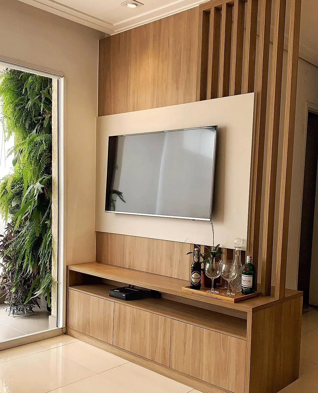 Painel de TV em madeira ripada com rack sob medida e jardim vertical na varanda – sala planejada Estillo Design Zona Leste