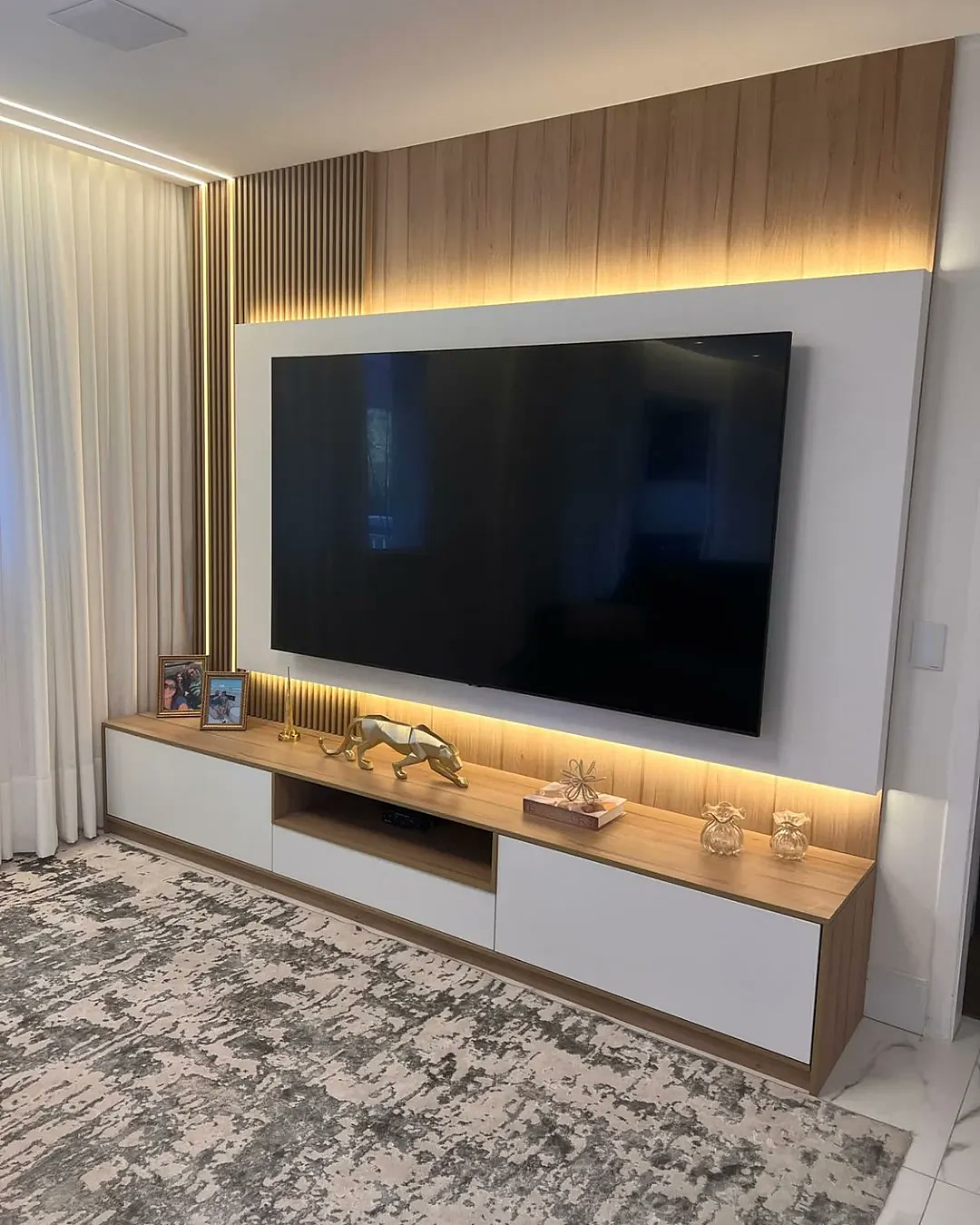 Sala planejada com painel de TV ripado em madeira, rack sob medida com gavetas brancas e iluminação LED – projeto residencial Estillo Design SP